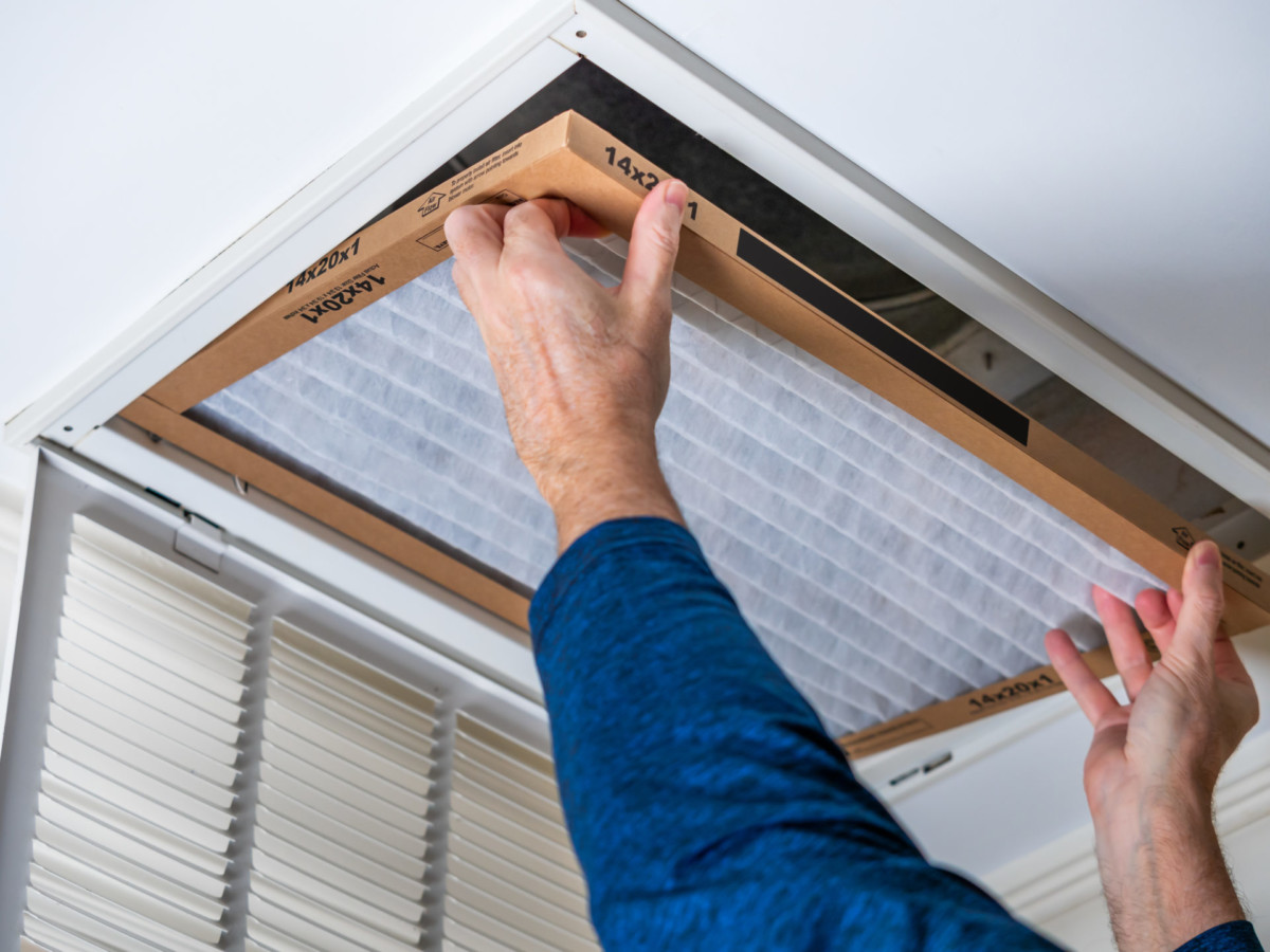 A person replacing an air filter in a ceiling hvac intake vent.