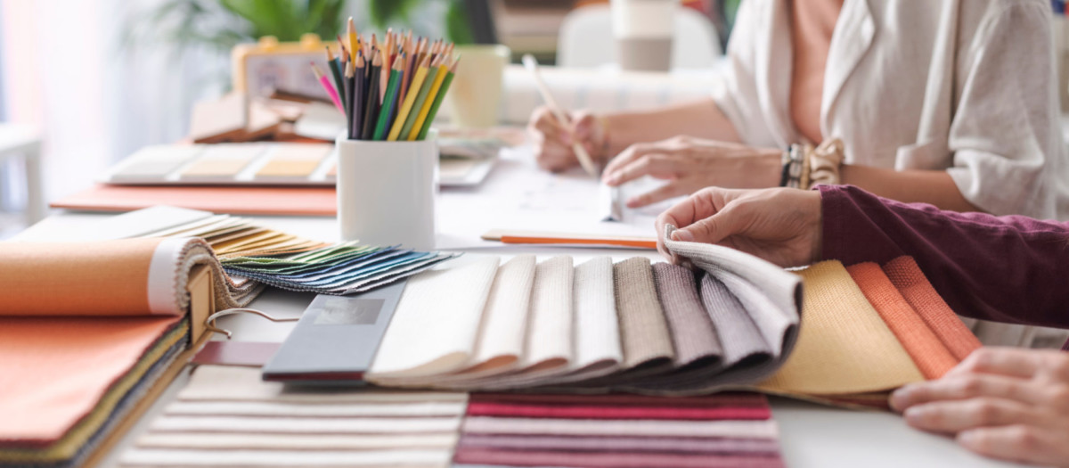 Designers discussing fabric options at a table covered with fabric swatches and color pencils.