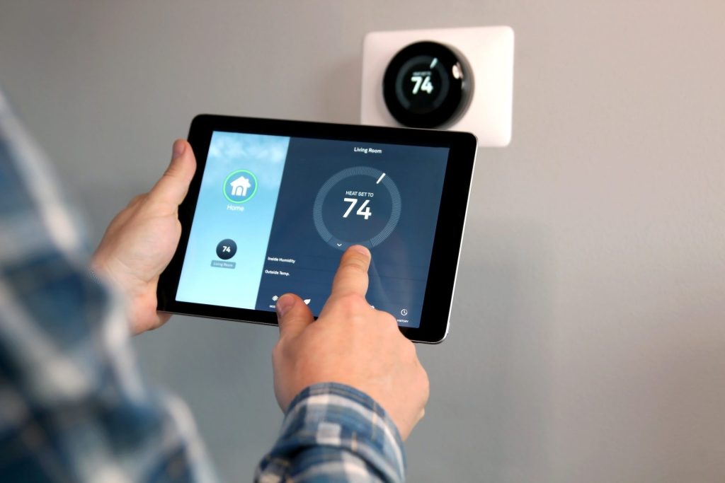 A person uses a tablet to adjust a smart thermostat, both displaying a temperature setting of 74 degrees—comfort and lower energy bills made easy with smart thermostats.
