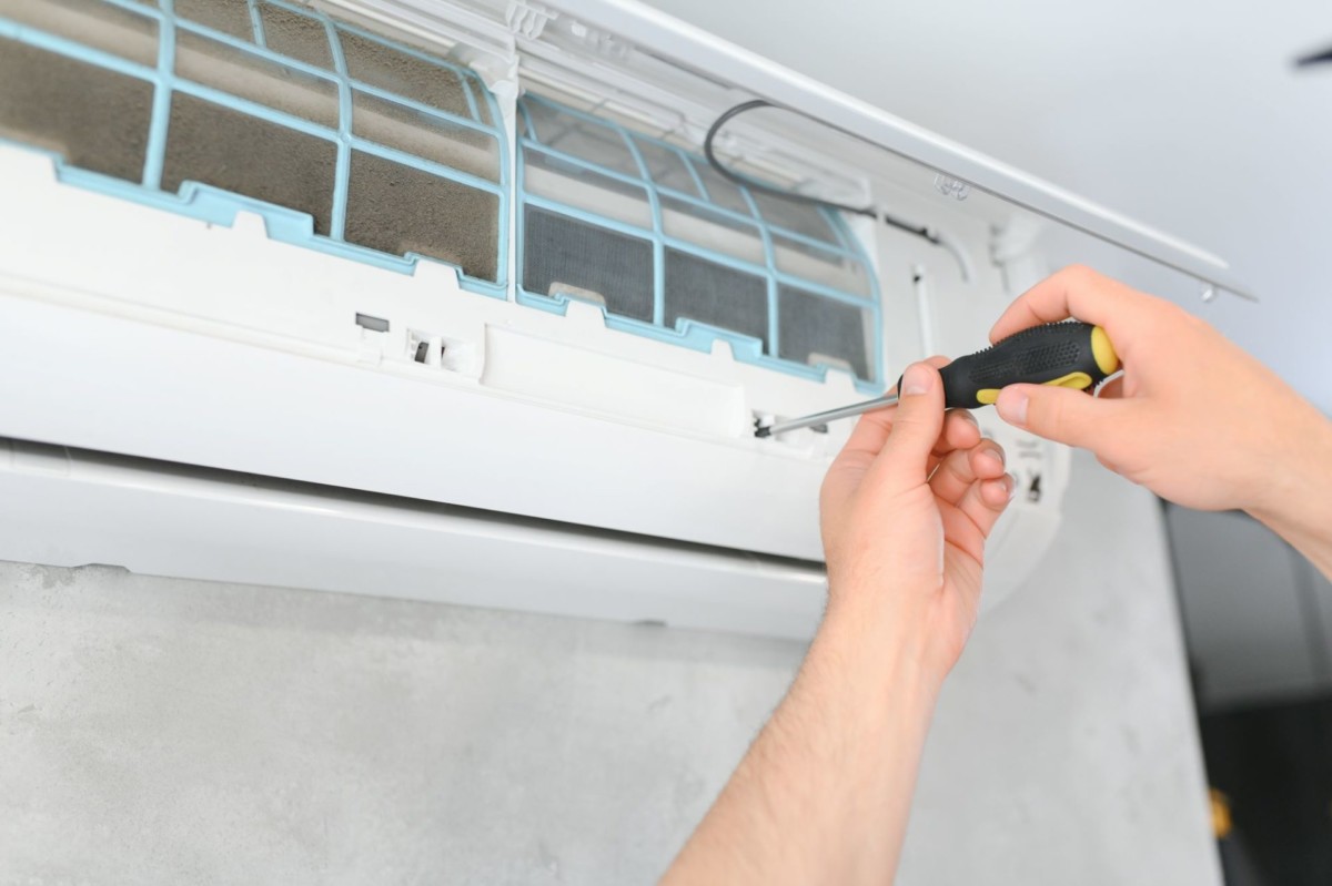 A person uses a screwdriver to perform maintenance or repairs on an open wall-mounted air conditioning unit after a heat pump breakdown. A person uses a screwdriver to perform maintenance or repairs on an open wall-mounted air conditioning unit after a heat pump breakdown.